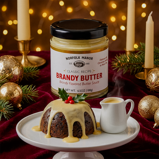 Christmas pudding with brandy butter sauce on a cake stand, jar of Norfolk Manor Brandy Butter, and festive decorations