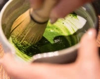 Person using a Matcha whisk to prepare matcha green tea in a small bowl.