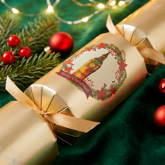 Close-up of a gold Christmas cracker with a lantern design, pine sprigs, and red baubles on green fabric