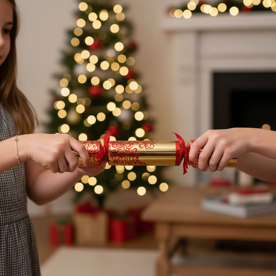 Two people holding a Christmas cracker with a decorated tree in the background