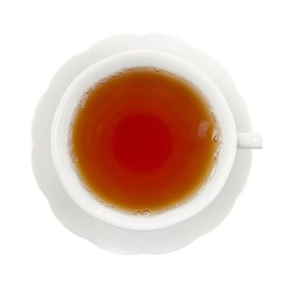 Top-down view of hot light amber colored tea in a white teacup on a white saucer all on a white background.
