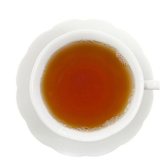 Top-down view of amber hot tea in a white teacup on a white saucer and on a white background.