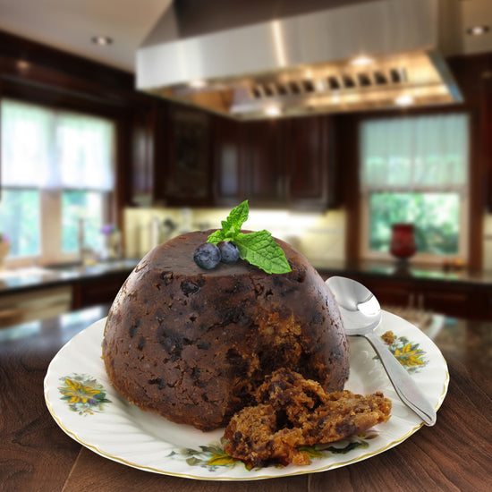 A Christmas Pudding baked desert on a floral plate with a sliver spoon. The item super imposed on the backdrop of a modern looking kitchen featuring steel and dark wood.