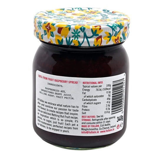 Back of a jar of Folláin raspberry jam with a floral lid on a white background with label displaying ingredients and nutrition