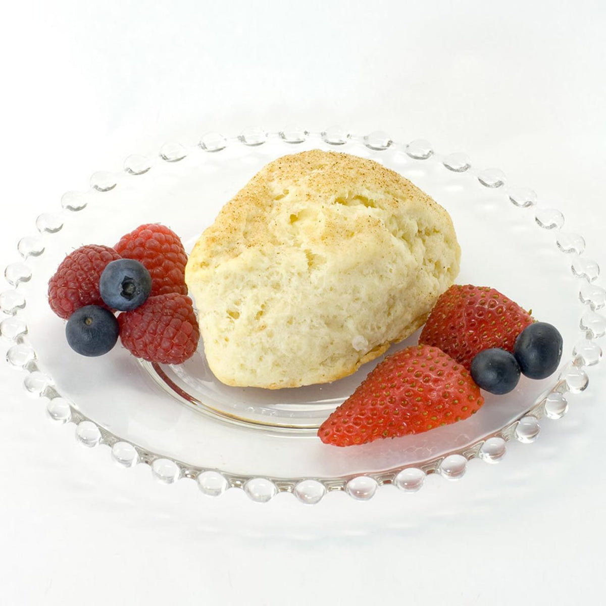 Baked English scone on a clear plate with fresh strawberries, raspberries, and blueberries