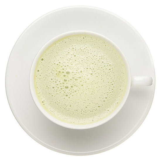 White cup of frothy green tea on a matching saucer against a white background