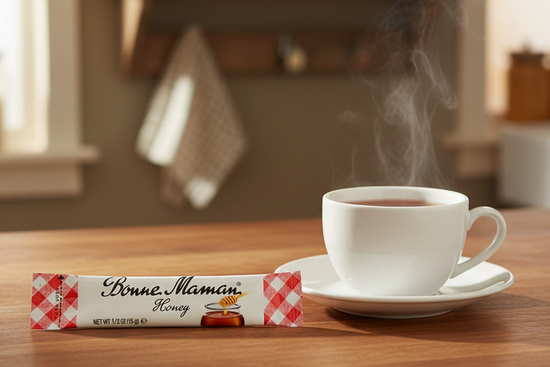 Bonne Maman honey stick with a steaming cup of tea on a wooden table