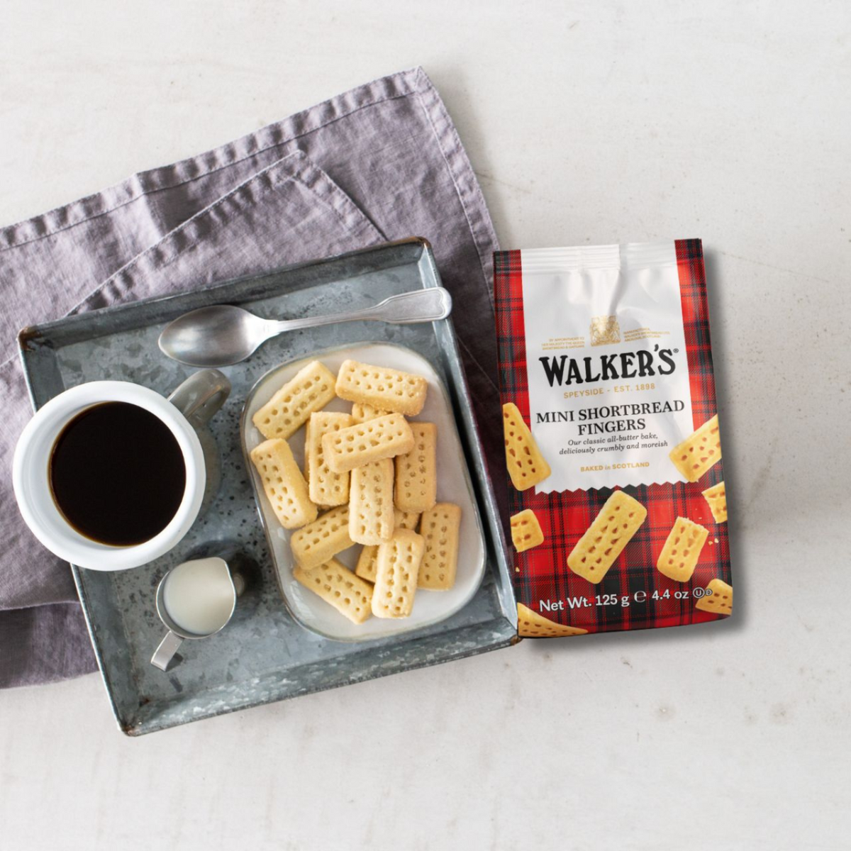Tray with Walker's Mini Shortbread Fingers, a cup of coffee, and a small container on a light background.