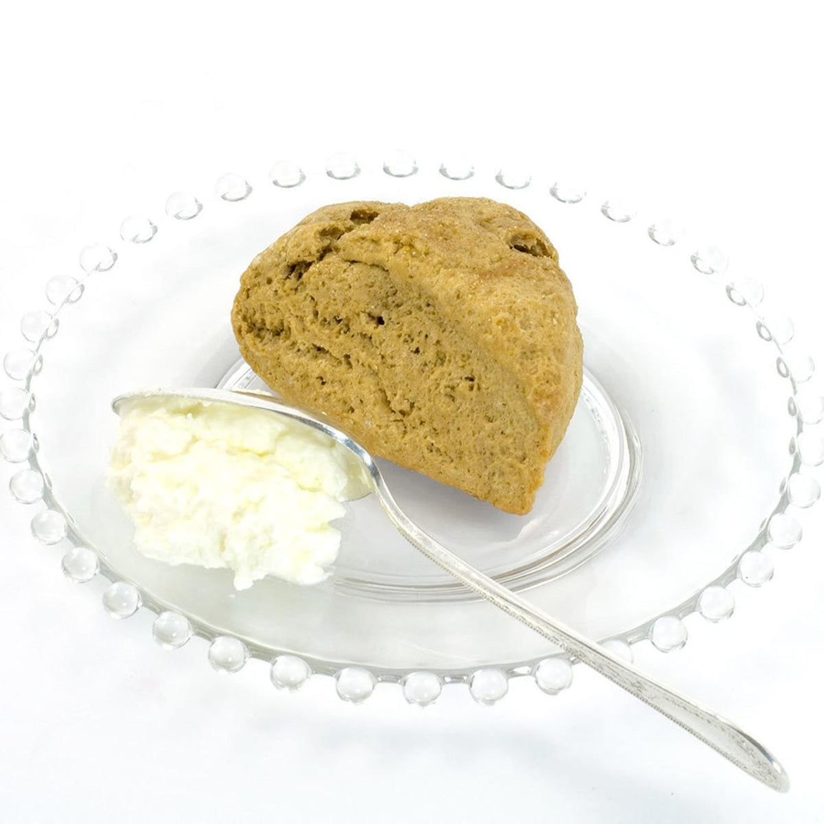 Baked scone with a side of cream on a white plate with a silver fork.