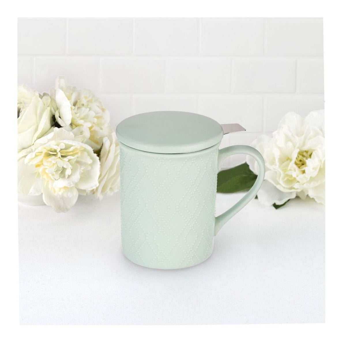 Mint green mug with lid on a white surface with white flowers in the background