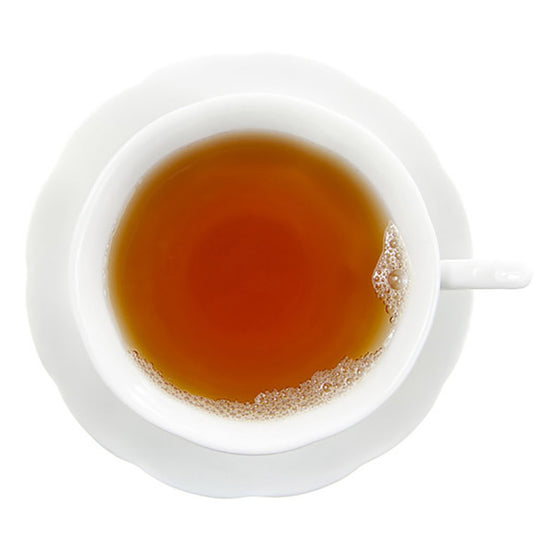 Top-down view of a white teacup filled with amber colored Earl Grey Cream tea with cup on a saucer all on a white background.