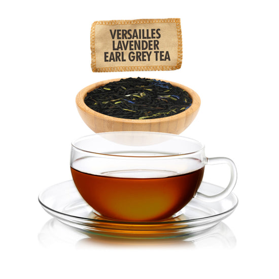 Amber colored tea in a clear mug and saucer on a white background with a wooden bowl of black tea, lavender petals and cornflower petals with a tag for the product name "Versailles Lavender Earl Grey Tea."