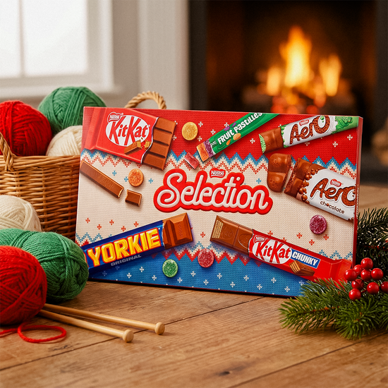 Nestlé Selection box on a wooden table with yarn, Christmas decorations, and a fire in the background
