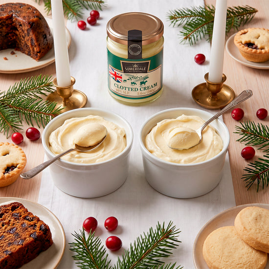 Two bowls of clotted cream on a table with mince pies, cranberries, and pine sprigs
