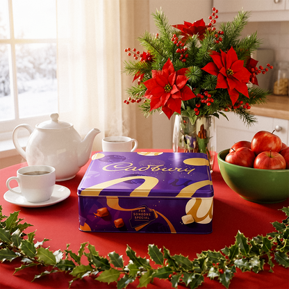 Cadbury gift box on a table with a teapot, cup, poinsettia, and bowl of apples