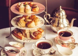 Three-tiered cake stand with pastries and teacups on a table with a teapot.