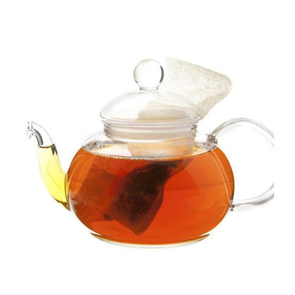 Glass teapot filled with light amber colored hot tea and a teabag.