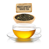 Clear glass cup of peach apricot white tea with tea bag and bowl of tea leaves on a white background.