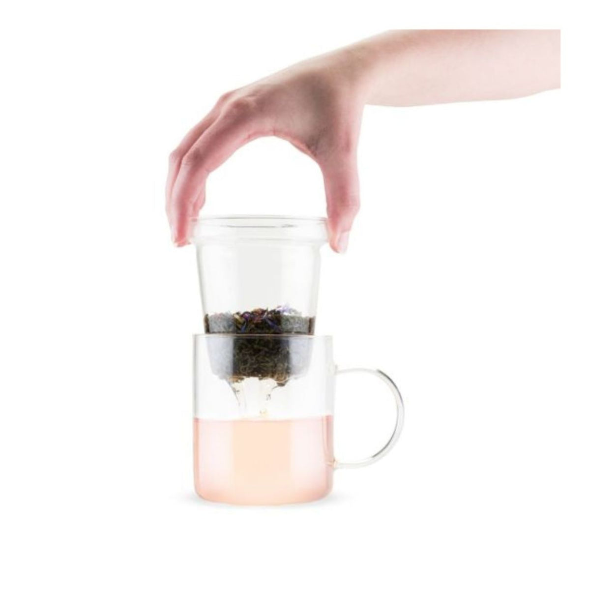 Hand holding a glass mug with a tea infuser on a white background