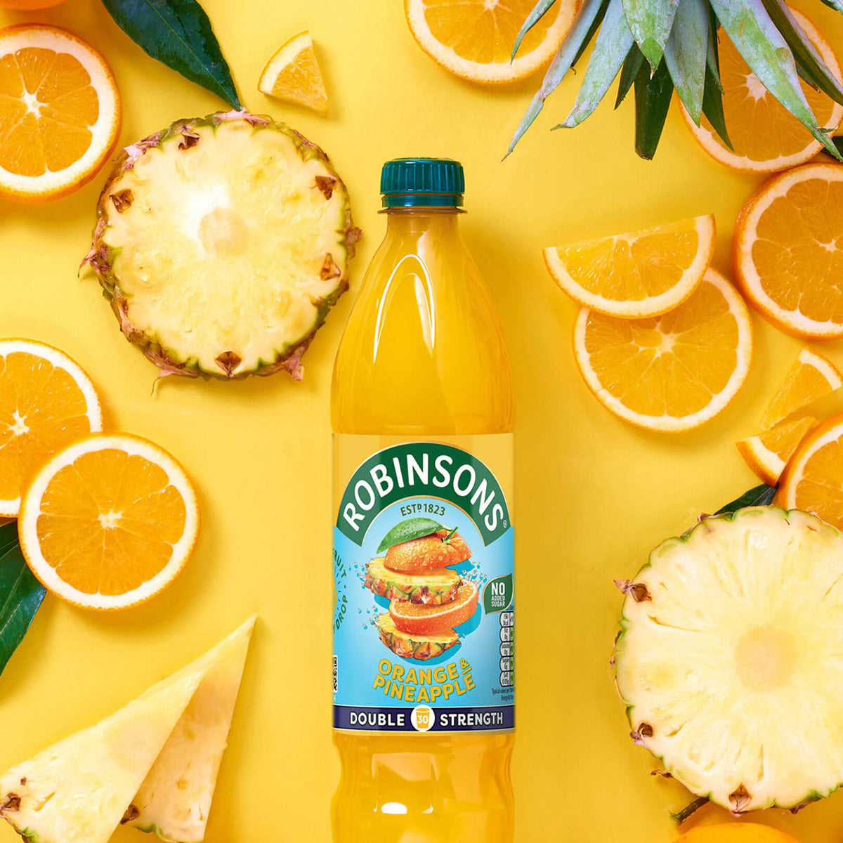 Robinsons Orange Pineapple juice bottle surrounded by oranges and pineapples on a yellow background