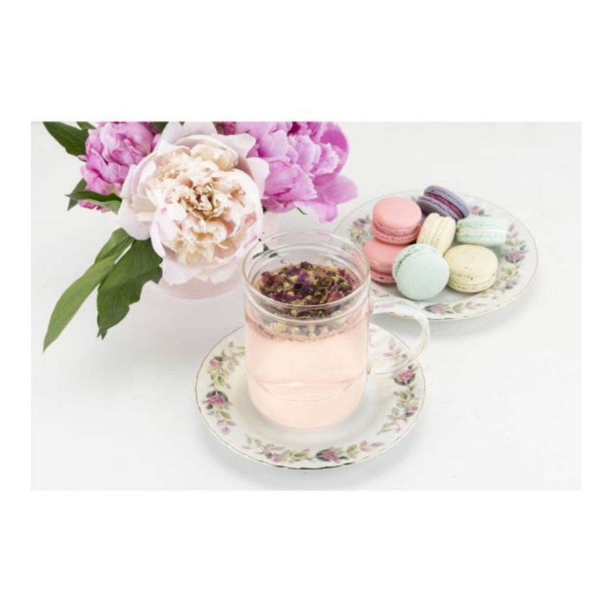 Glass of pink tea with a flower, macarons, and flowers on a white background