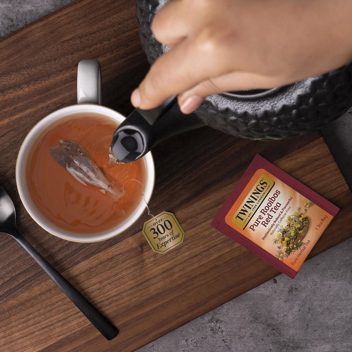 Tea being poured into a cup with a Twinings tea bag and packaging on a wooden surface.