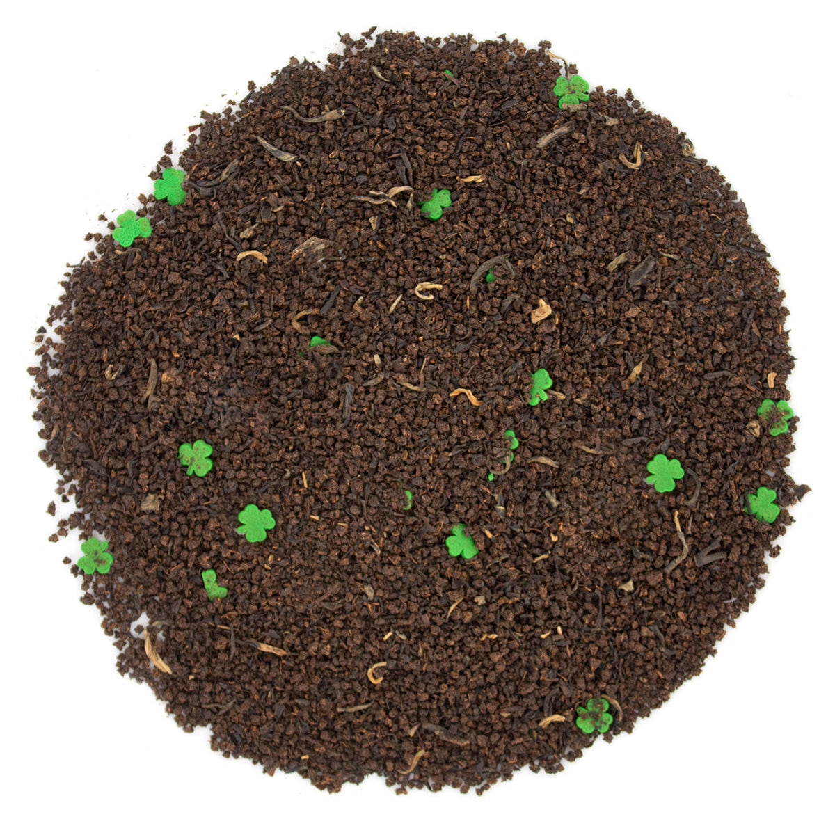 Round piece of black loose-leaf tea with small green shamrock shaped candy pieces on a white background