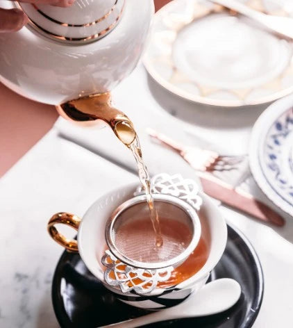 Tea being poured from a teapot into a cup with a decorative handle on a marble surface.