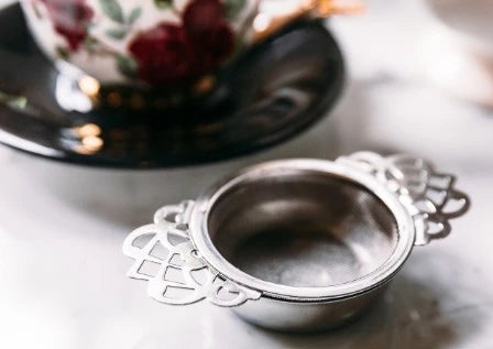 Silver tea strainer on a table with a teacup in the background