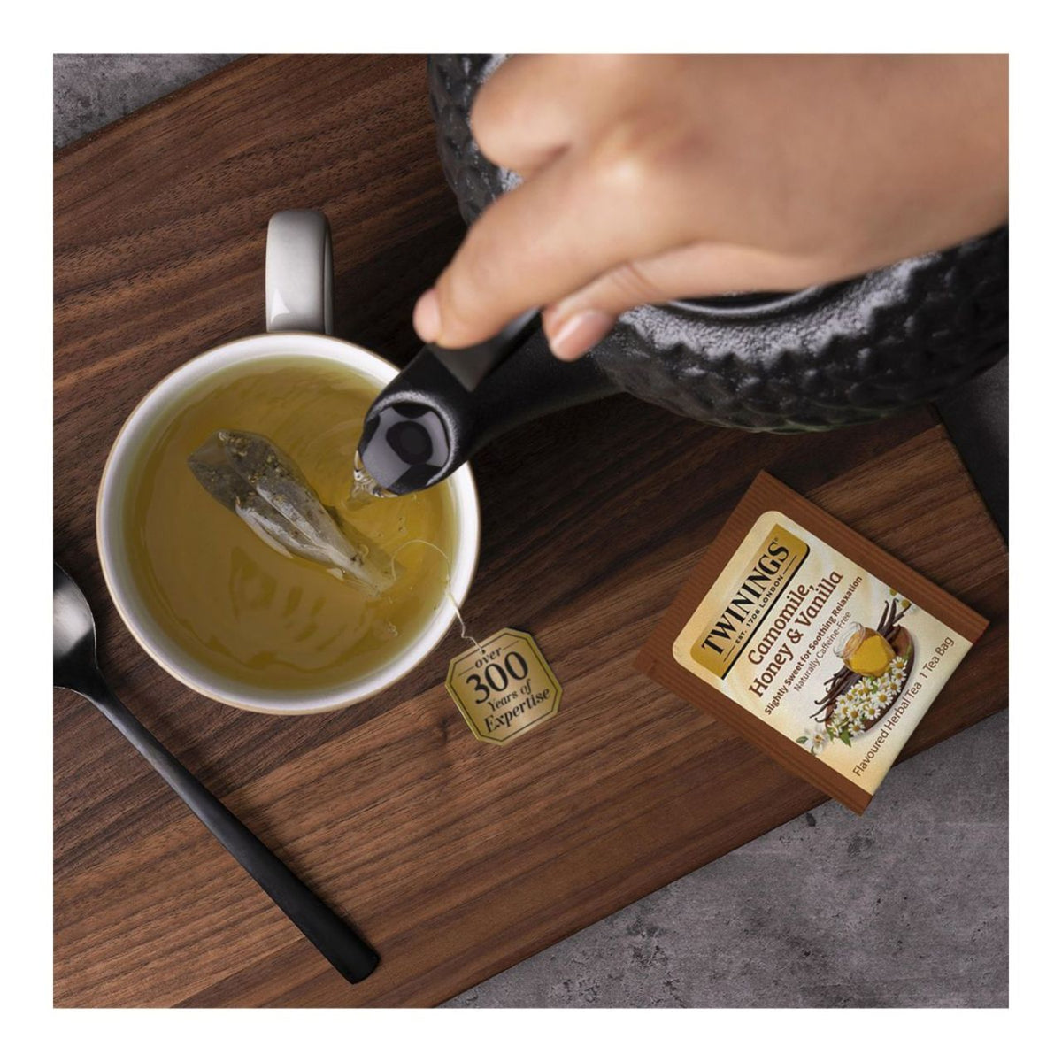 Tea being poured into a cup with a Twinings tea bag and box on a wooden surface.