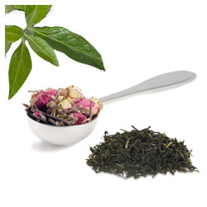 A spoon with tea leaves and floral petals on a white background with a small pile of dry black tea leaves on the side