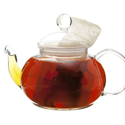 Clear glass teapot with a lid filled with dark amber with red tint liquid tea with a teabag with the teapot on a white background