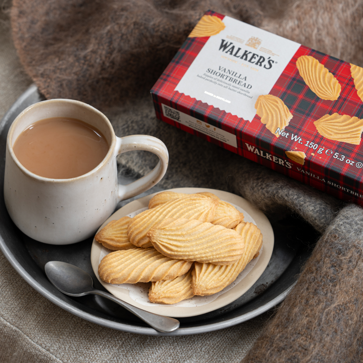Walkers Vanilla Shortbread cookies on a plate with a cup of tea and the cookie box in the background.