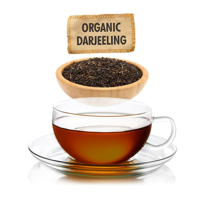 Glass cup of organic Darjeeling tea with tea leaves in a wooden bowl and label above.