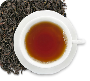 Black tea leaves on a checkered black and grey background and the center contains a top down view of a white teacup filled with dark amber black tea on a white saucer.