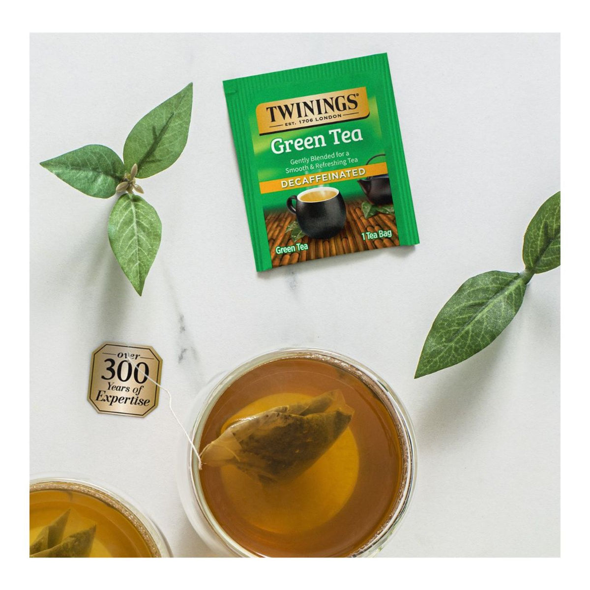 Twinings green tea package with a cup of tea and tea leaves on a white background