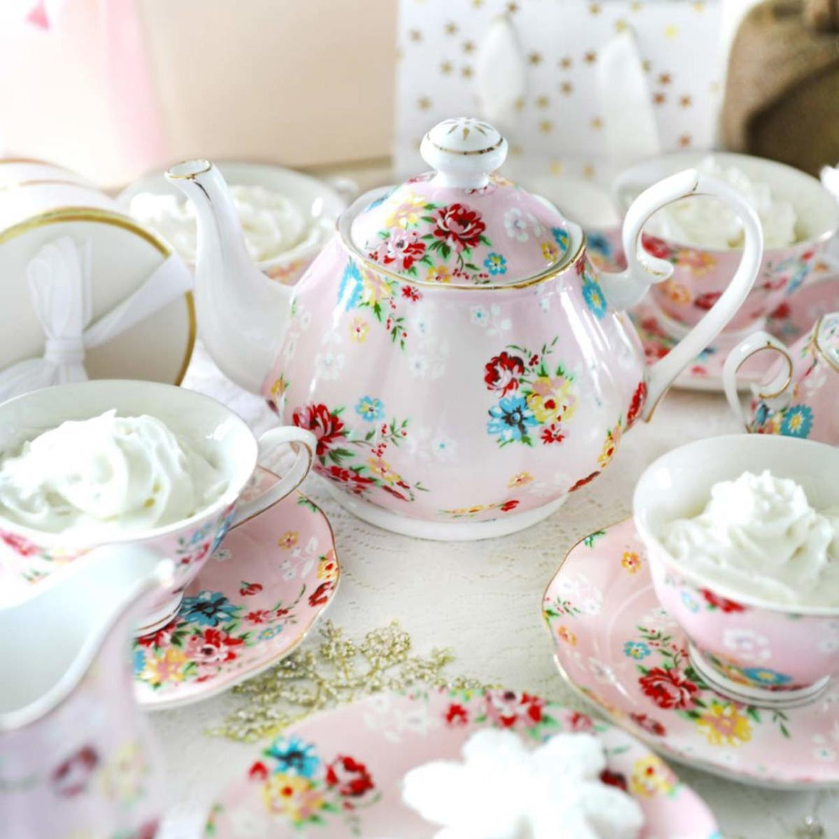 Shabby Rose Pink Porcelain floral teapot and cups with whipped cream on a decorative tablecloth.