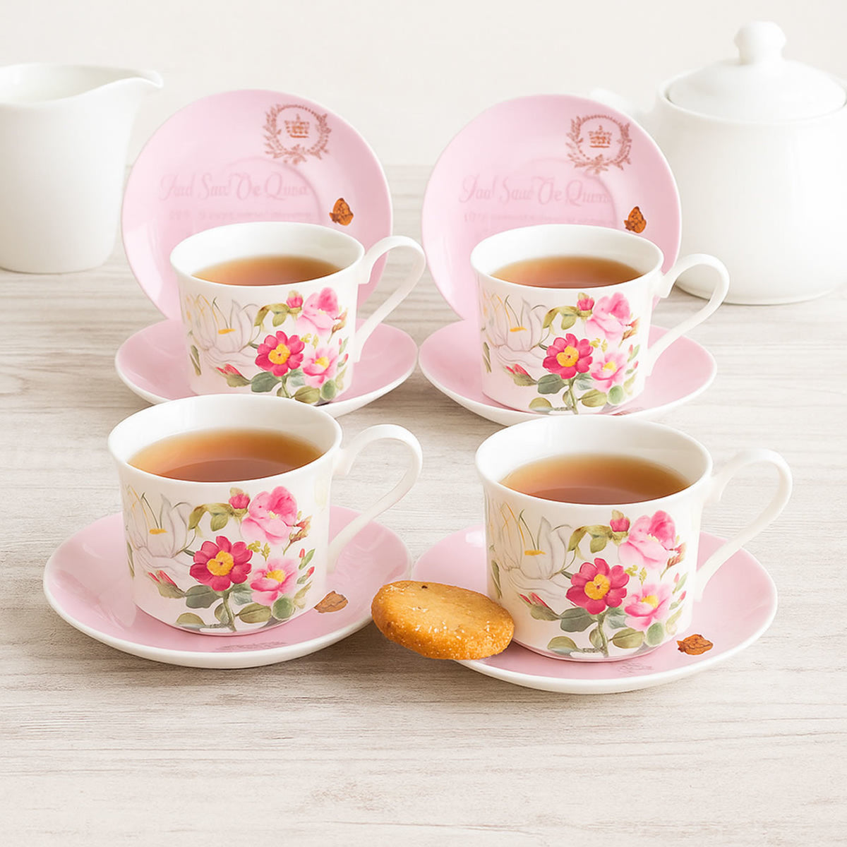 Set of four floral teacups and saucers with pink borders on a light wooden surface.