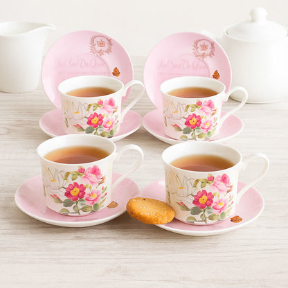 Set of four floral teacups and saucers with pink borders on a light wooden surface.