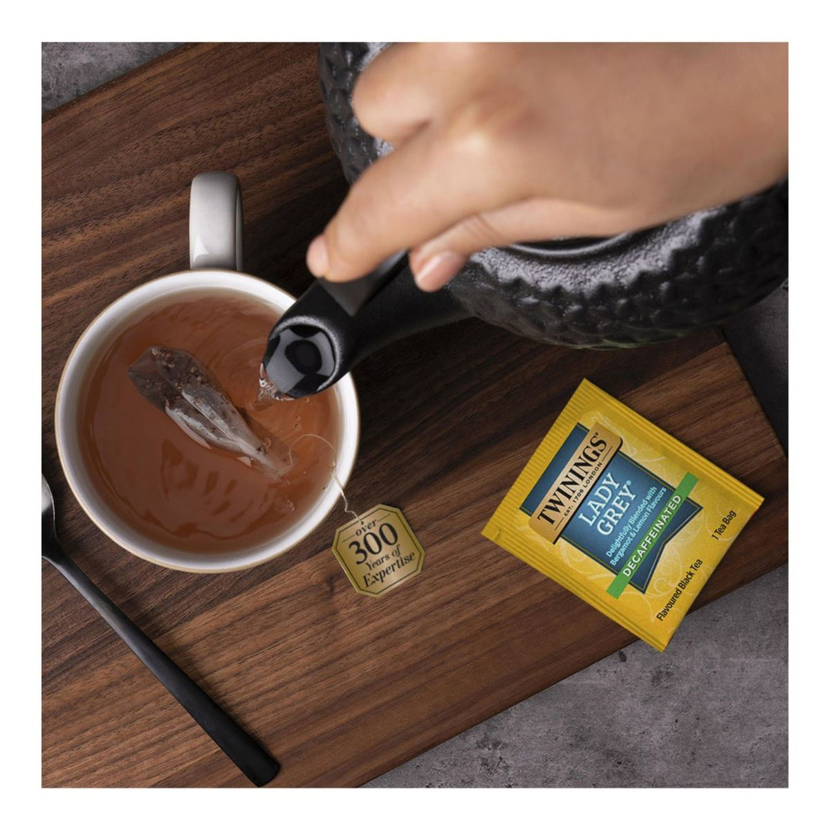 Tea being poured into a cup with a Twining's Lady Grey tea bag on a wooden surface.