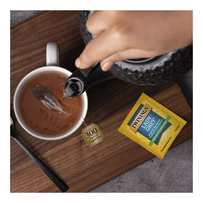 Tea being poured into a cup with a Twining's Lady Grey tea bag on a wooden surface.
