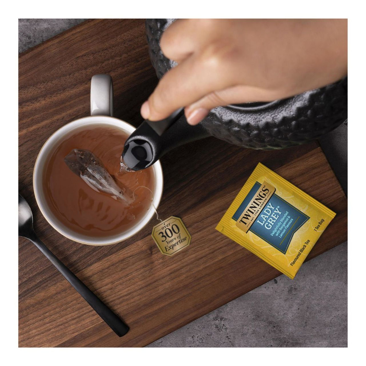 Tea being poured into a cup with Twinings Lady Grey tea bag on a wooden board.