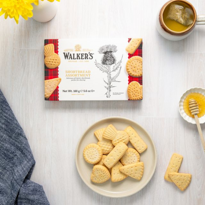 Box of Walker's Shortbread Assortment on a table with cookies on a plate and a cup of tea.