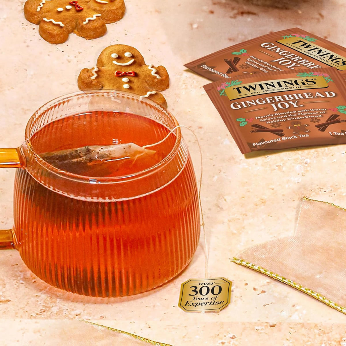 Glass teapot with gingerbread-themed tea and gingerbread cookies on a textured surface