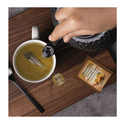 Tea being poured into a cup with a Twinings Orange & Cinnamon Spice tea box on a wooden surface.
