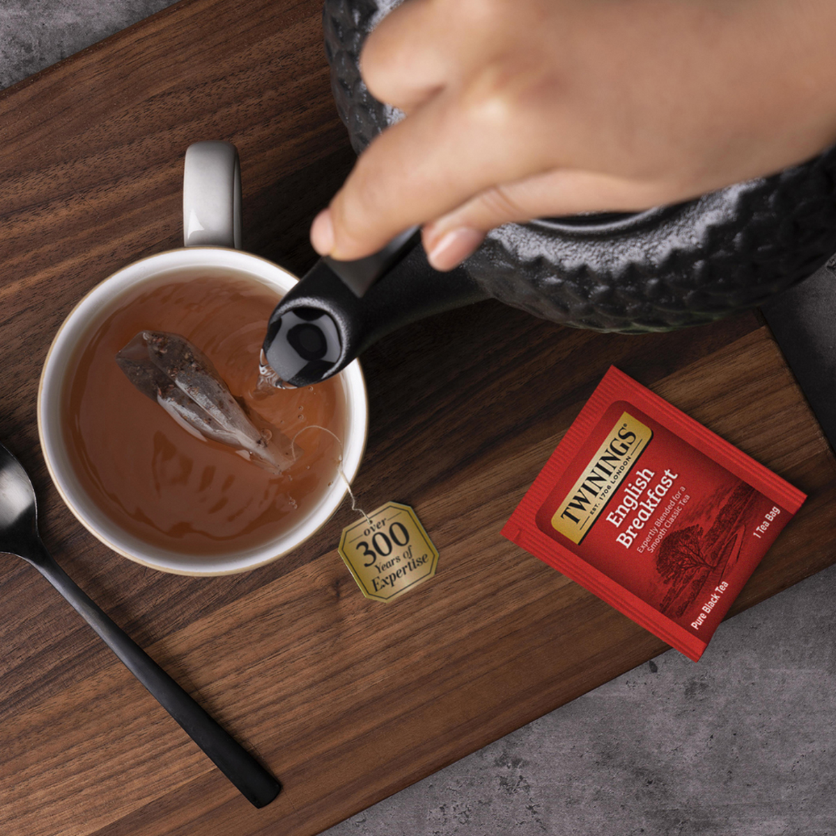 Tea being poured into a cup with a Thynnels English Breakfast tea bag on a wooden surface.