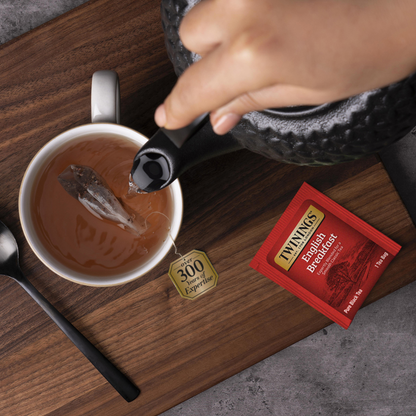 Tea being poured into a cup with a Thynnels English Breakfast tea bag on a wooden surface.