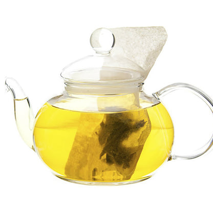 Clear glass teapot with yellow colored hot tea and a tea bag on a white background
