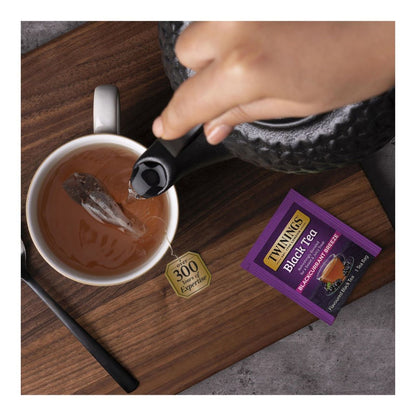 Tea being poured into a cup with a Twining's Purple colored Baclkcurrant Breeze Black tea bag on a wooden surface