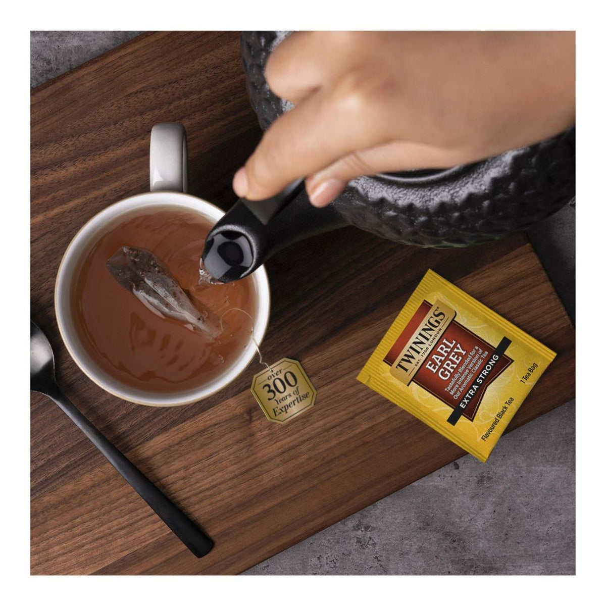 Person pouring tea into a cup with Twinings Earl Grey tea bag on a wooden surface.
